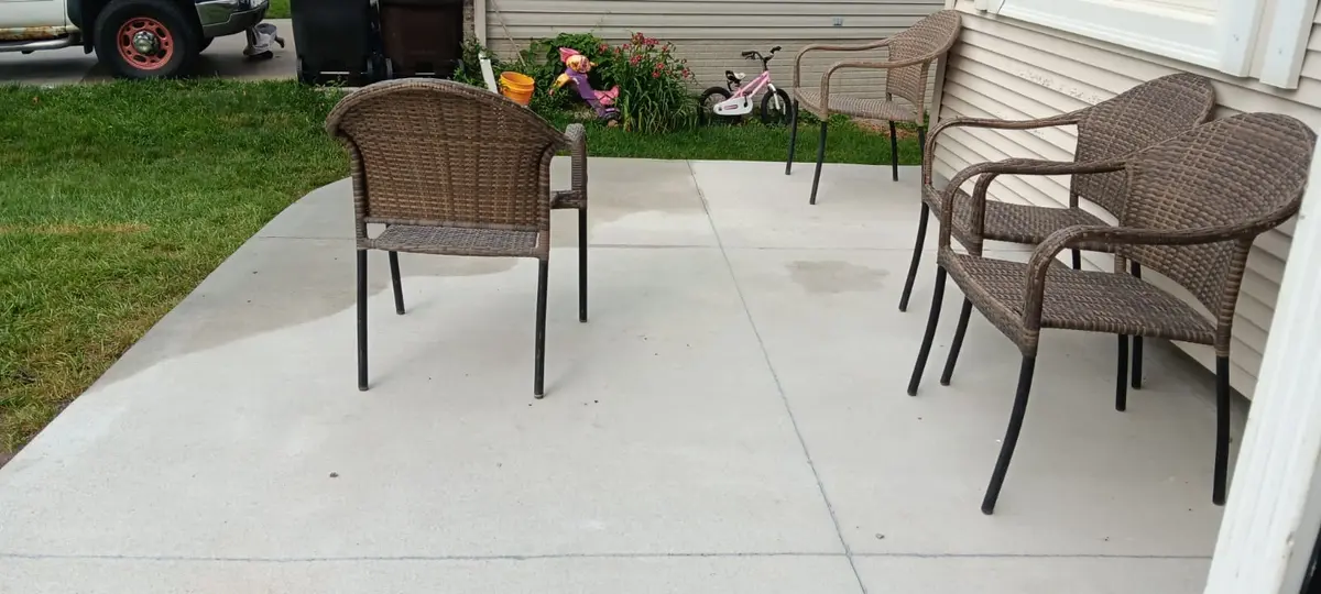 A finished broom-finish concrete patio beside a house, with outdoor chairs set out on it.
